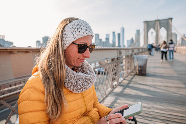istock Woman in Yellow Jacket Using Smartphone on Brooklyn Bridge 2207025601