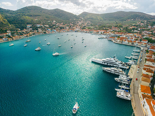 Aerial view of sailboats and yachts anchored in a beautiful bay of Vathi, Ithaca, Greece. There are small, traditional Mediterranean houses near waterfront. It's a beautiful sunny summer day, the sea is blue, green and turquoise.