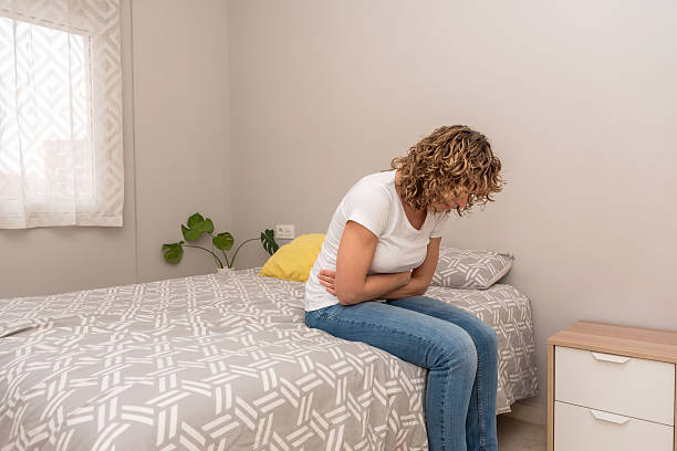 istock Woman feeling intense abdominal pain while sitting on the bed, possibly due to menstruation or indigestion 2207027725