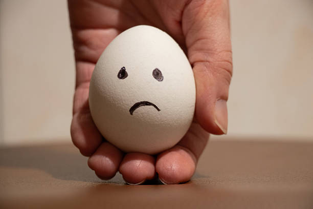 Woman holding chicken egg in hand with sad and sorrowful emotions drawn on egg, egg shortage in 2025