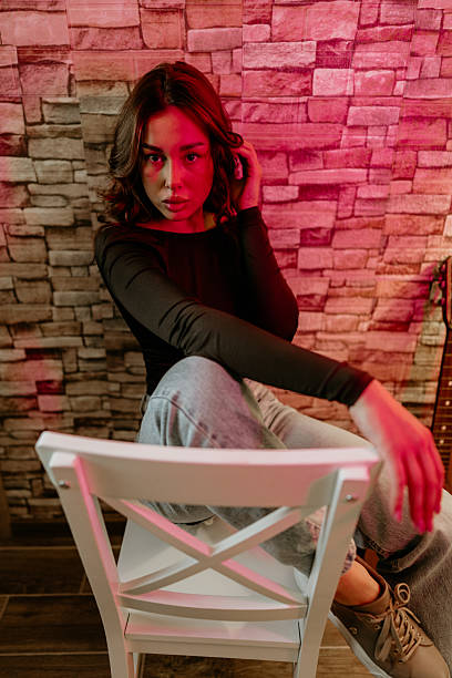 A young, attractive model kneeling and posing under red neon lights in an indoor parking lot.