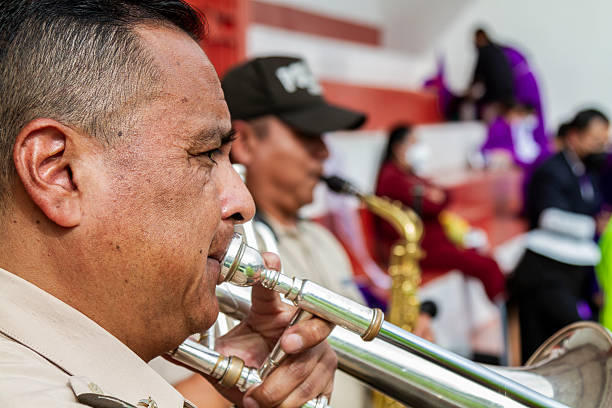 Quito, Pichincha, Ecuador - April 15, 2022: Close-up of a musician playing a trombone during a traditional religious procession, with other musicians and people in traditional purple robes in the background