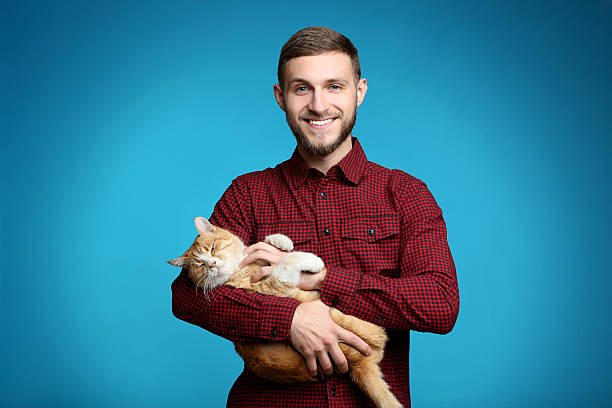 Portrait of young man with ginger cat on blue background