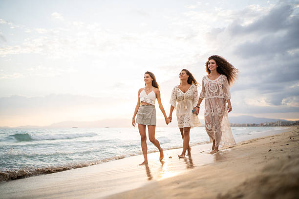 istock Three women holding hands and walking on the beach at sunset 2207034591