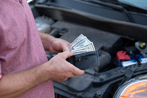 Man holds dollar bills while assessing car repairs with determination
