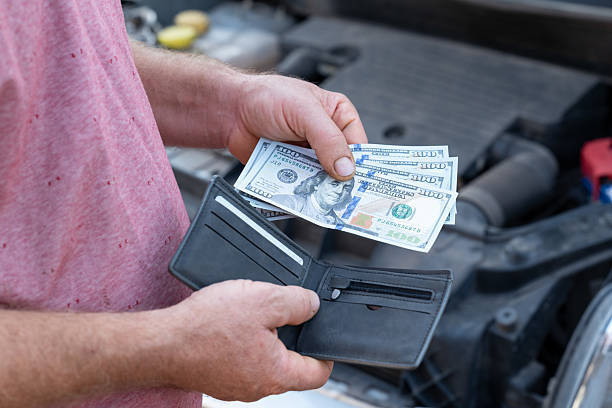 istock Man counts cash while standing beside a car in a parking area 2207035645