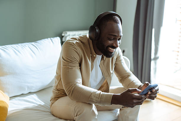 istock Man wearing headphones smiling while using a smartphone in a relaxed setting 2207037868
