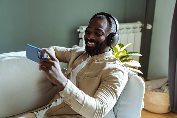 istock Man relaxing on couch with headphones while watching video on smartphone 2207038446