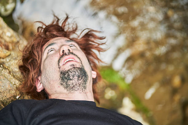 Injured hiker with a dirty face and messy hair is lying on the ground looking up, possibly after a mountain accident, conveying a sense of vulnerability and distress