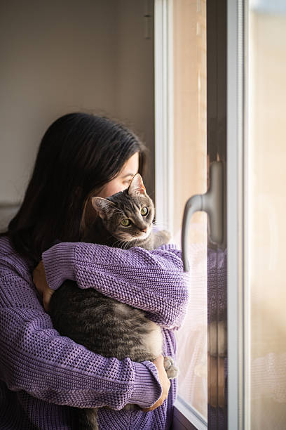 istock Young woman embracing her cat while looking out the window 2207040723