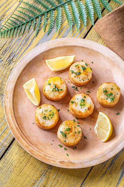 Tender fried scallops in butter served with lemon, parsley, rustic yellow background