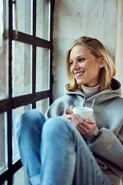 istock Smiling Woman Relaxing by Window Holding Coffee Cup in Cozy Setting 2207047457