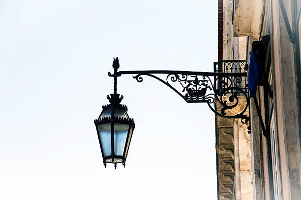 An ornate, wrought iron street lamp is mounted on the side of an old building, casting a striking silhouette against a clear sky. The decorative metalwork features intricate details that add an element of elegance. Taken in Lisbon, Portugal.