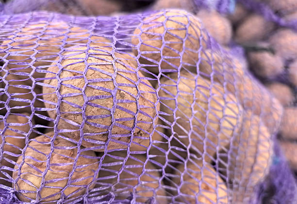Vendors display fresh potatoes in mesh bags at a bustling market.