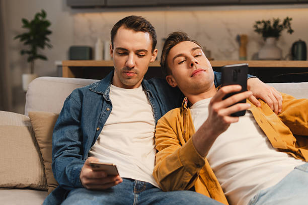 istock Handsome, attractive gay couple relaxing on sofa and using smartphones 2207060067