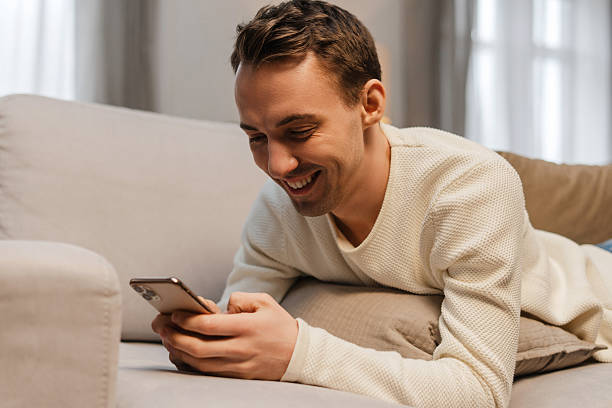 istock Smiling, happy man holding mobile phone, using mobile app, lying on comfortable sofa at home 2207060096