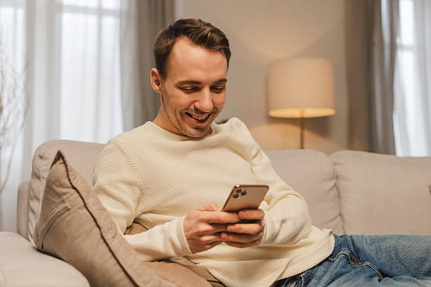 istock Smiling man relaxing on sofa using smartphone smiling and enjoying social media 2207060100