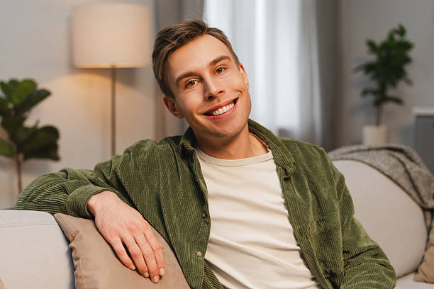 istock Young, happy man smiling and relaxing on sofa at home looking at camera 2207060118