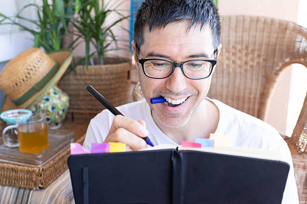 istock Smiling man writing on a journal and holding a pen in his mouth 2207061164