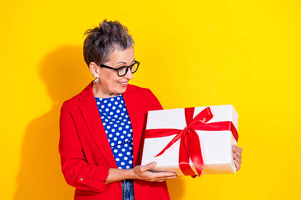 istock Charming middle-aged woman holding gift box against vibrant yellow background, combining stylish fashion and joyful emotion 2207061867
