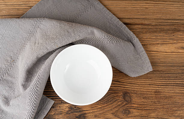 Empty white bowl on table, porcelain plate on wooden tabletop and grey tablecloth, minimal dish mockup on cloth napkin fabric, rustical kitchen banner with copy space for text top view