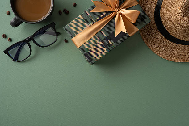 istock Gift box with ribbon, stylish hat, coffee mug, and glasses arranged on green surface 2207067787