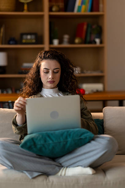 istock Young woman sitting cross-legged on a sofa, working from home using a laptop 2207068857