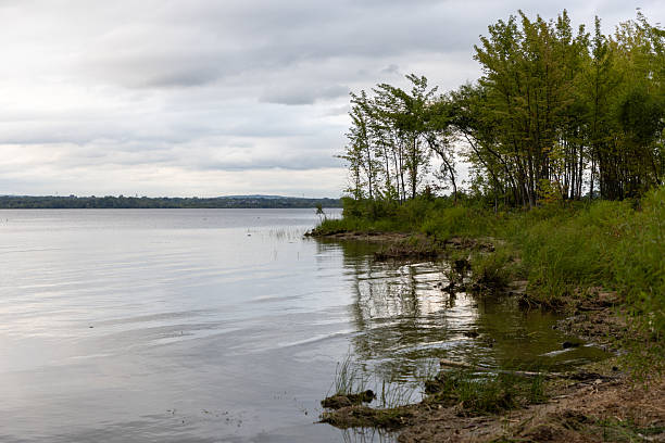istock River bank with cloudy sky. Waterfront landscape and skyline. Riverside with trees in summer 2207070573