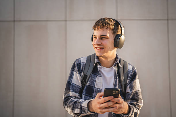istock young man student stand in front white wall and listen music 2207071388