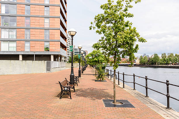 istock Harbourside footpath lined with benches and street lights on one side and trees on the other side on a sunny day 2207071523