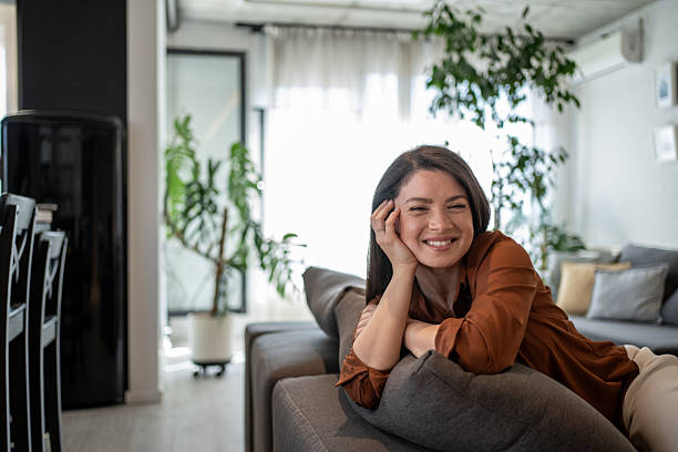istock Happy woman relaxing on sofa at home smiling at camera 2207075903