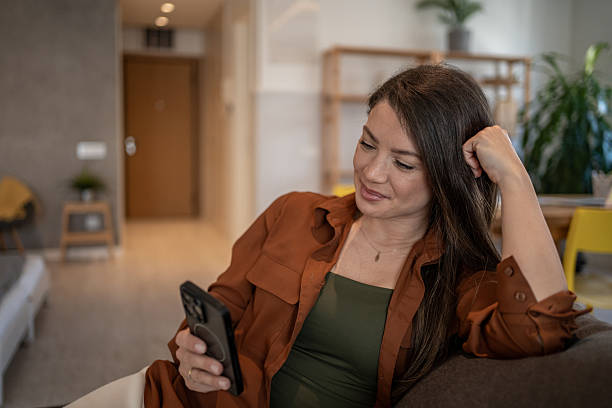istock Smiling woman relaxing on sofa using smartphone at home 2207076043