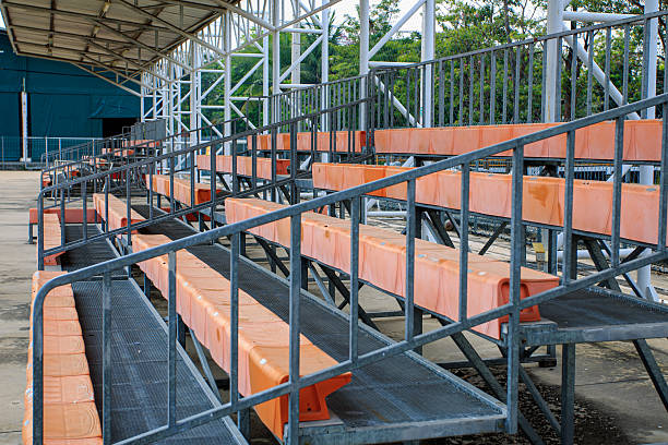 The stadium is empty with no one sitting on the bleachers. The bleachers are orange and there is a blue building in the background