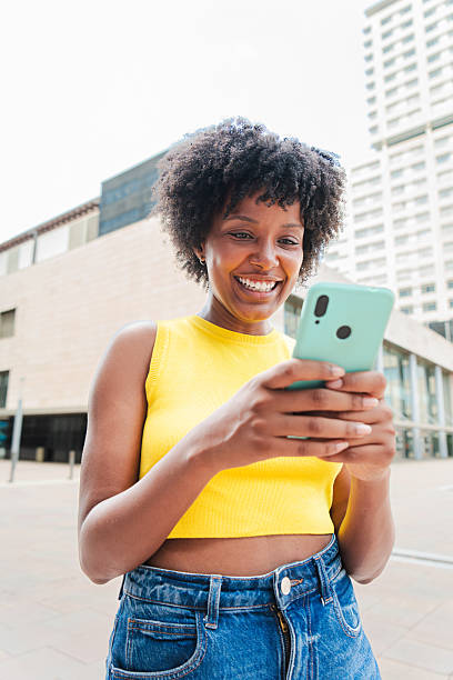 istock Vertical. African american girl smiling using a cellphone to browse on internet with an app. Teenage girl sharing photos on the social media with a mobile phone. Young woman holding a smartphone 2207085202