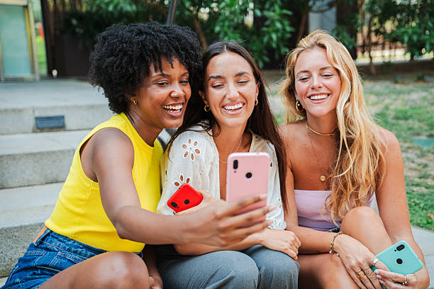 istock Three joyful young women enjoying a fun moment together while taking selfies with their smartphones, sharing laughter and happiness in a delightful social interaction with friendship and connection 2207086264