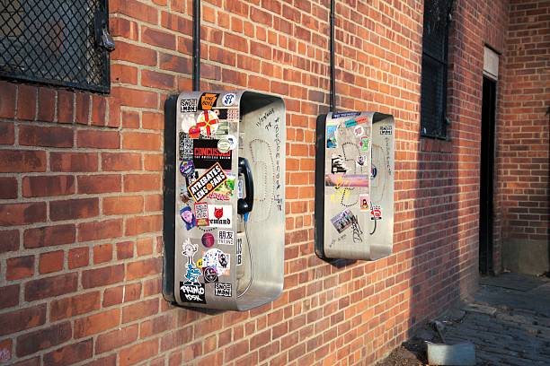 Profile angle of two public phone receptacles mounted on a brick wall and covered with stickers. Taken while walking in Central Park, New York City on a clear winter day.