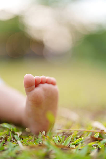 Close-up of a one-year-old baby girl's foot resting on green grass, bathed in warm outdoor sunlight with soft background bokeh.