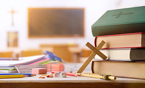 Educational supplies and religious objects on table with classroom background stock photo