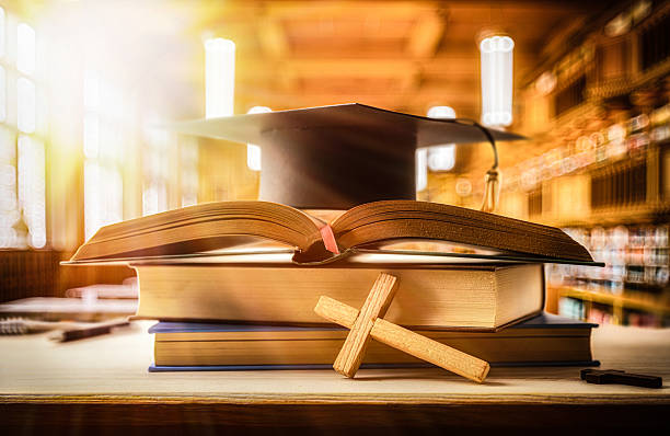 Stack of books with Bible and mortarboard in a classroom stock photo