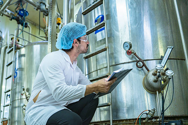 istock Technician in protective gear evaluating a production tank, representing quality assurance, meticulous processes, and expertise in industrial manufacturing. 2207100524