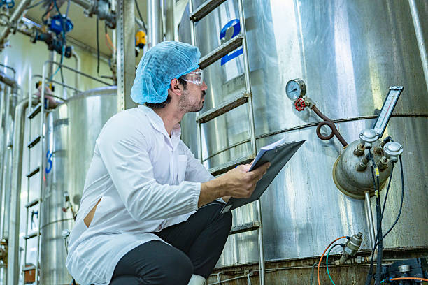 istock Technician in protective gear evaluating a production tank, representing quality assurance, meticulous processes, and expertise in industrial manufacturing. 2207100962