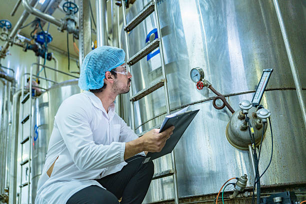 istock Technician in protective gear evaluating a production tank, representing quality assurance, meticulous processes, and expertise in industrial manufacturing. 2207101283