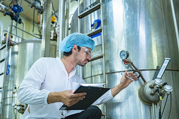 istock Factory technician inspecting an industrial tank with a clipboard, showcasing precision, quality control, and attention to detail in a modern manufacturing environment. 2207101748