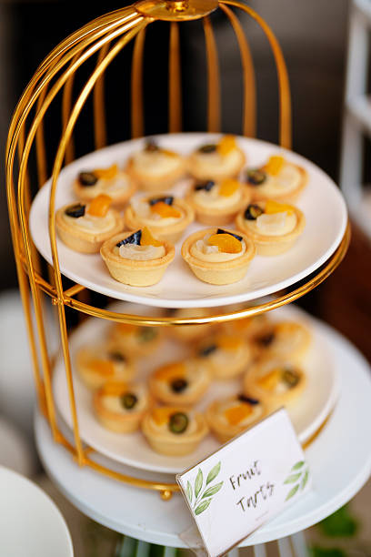 Close-up of colorful mini fruit tarts arranged on a stylish gold-tiered dessert stand, topped with assorted fresh fruits like grapes, peaches, and pears.