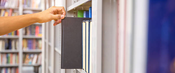 istock Book and library, Close up hand choosing and picking books from bookshelf in library. Concepts of reading textbook and school for student knowledge education or study and learning 2207105466