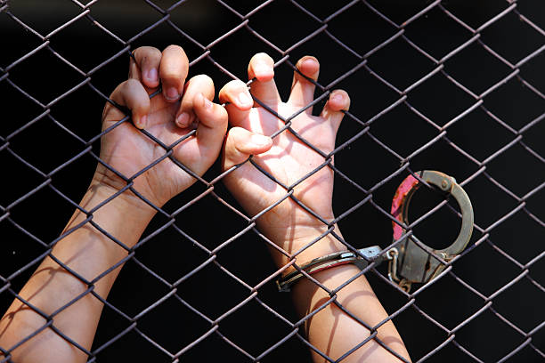 Hands Grasping Metal Fence Behind Chain Link Barrier in Dramatic Light