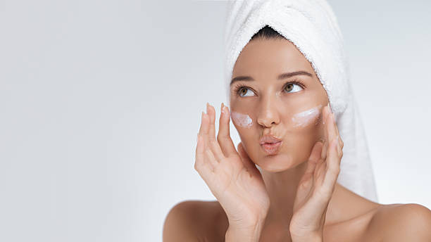 istock Playful Woman Applying Face Cream With Towel on Head 2207115701