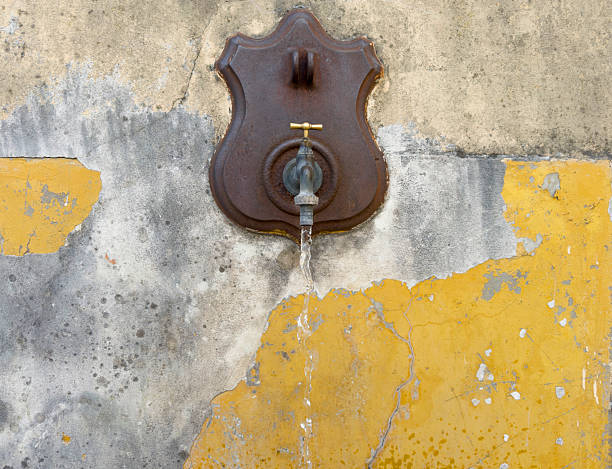 istock Rustic Public Fountain with Water Flowing on Yellow Wall. 2207121059