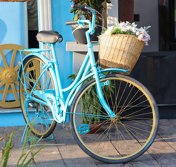 A blue bicycle with a basket full of flowers. The basket is full of flowers and the bike is parked outside