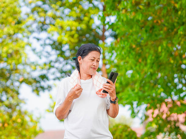 istock senior woman enjoying an outdoor workout, smiling while using mobile phone, smartwatch 2207124350